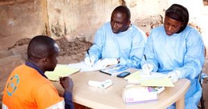 Souare Sekouba (l), and Conde Doussou, (r) part of the WHO vaccine trial teams, run a final follow up with a participant. Courtesy WHO